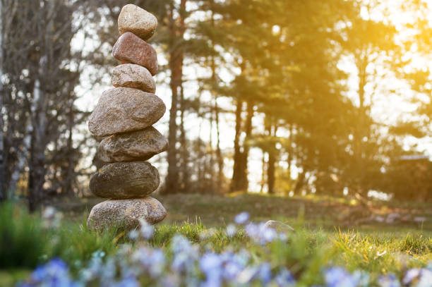 Balancing tower of large stones standing on top of each other on background of trees and spring flowers in sun. Calmness and relaxation concept